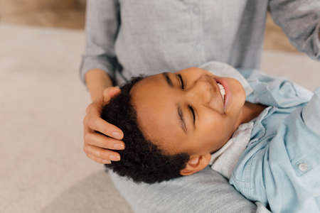 Boy resting at the knees of his caucasian mother while staying at homeの写真素材