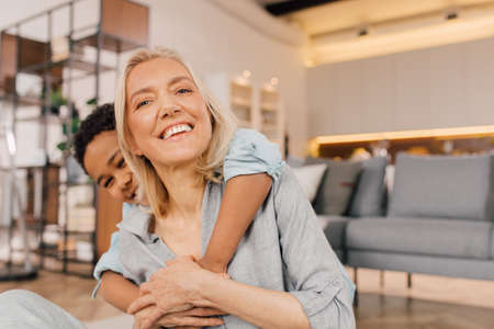 Mother looking at the camera while her multiracial son embracing herの写真素材