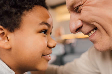 Boy looking at the eyes of his grandfather while spending time with him at homeの写真素材