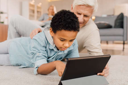 Dad and child laying at the floor, relaxing and having fun with tablet