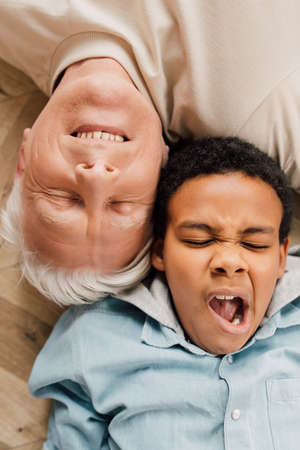 Boy yawns while laying at the floor near his grandfatherの写真素材