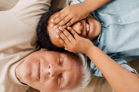 Boy closed his eyes with hands while laying at the floor near grandfatherの写真素材