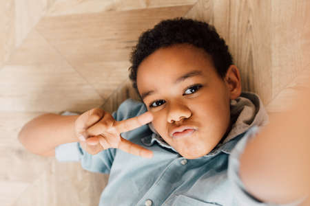 Boy resting at the floor and showing victory gesture to the cameraの写真素材