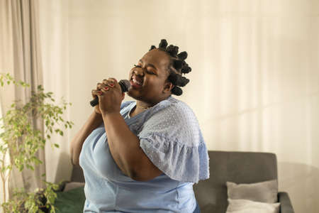 Woman holding microphone and singing a song at homeの写真素材