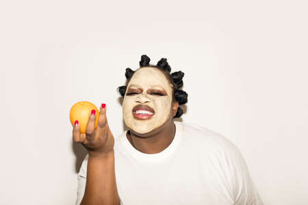 Woman with moisturizing mask at her face holding orange fruit and smilingの写真素材