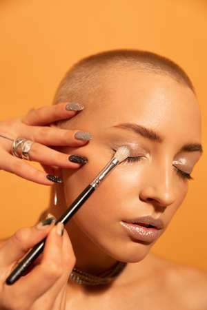 Woman standing in front of yellow wall while stylist preparing makeup for herの写真素材