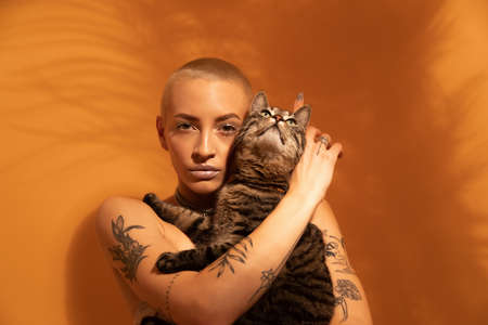 Woman posing in front of the yellow wall with her striped cat at the hands