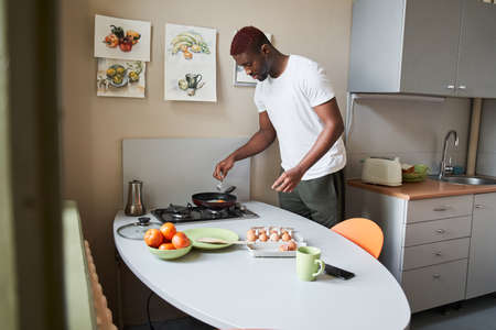 Man fries eggs at the frying pan while making breakfast at the little kitchen
