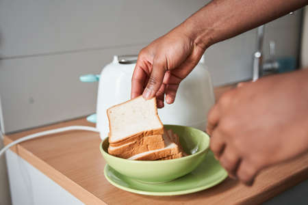 Man taking white toast bread from the plate during the breakfast