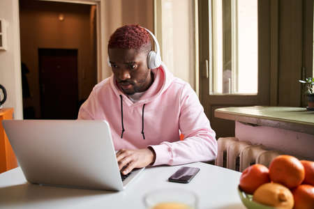 Student in headphones looking at the laptop screen while watching online lesson in the kitchenの写真素材