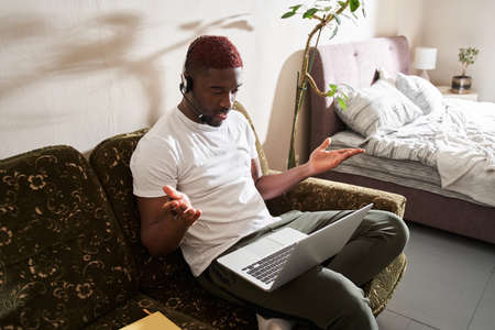 Employee in headphones looking at the screen and gesturing while using laptop
