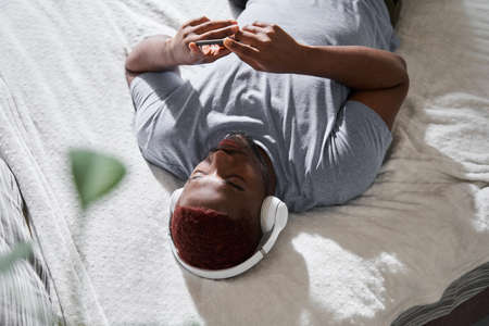 Man wearing headphones laying at the bed and listening music while switches songs