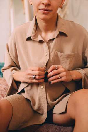 Girl with short haircut sitting at the bed and buttoning up her shirt