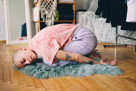 Woman with short hair laying at child pose while doing yoga on the wooden floorの写真素材