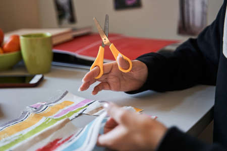 Woman holding scissors and cutting a piece of the fabric while sewing at the table