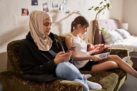 Girl looking at her smartphone with a pleasure smile while her caucasian bestie sitting nearby