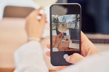 Close up shot of girl taking photo of laptop with by phone in restaurantの写真素材