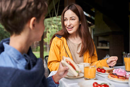 Charming young woman having breakfast with son outdoors