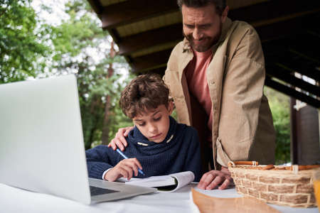 Cheerful father helping son to do homework outdoorsの写真素材