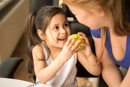 Child treats her caucasian mom with an apple while doing homework and learningの写真素材