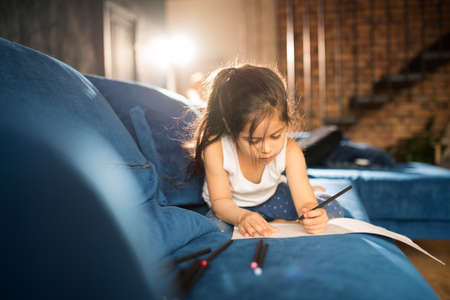 Girl laying at the sofa and drawing greeting picture for her motherの写真素材