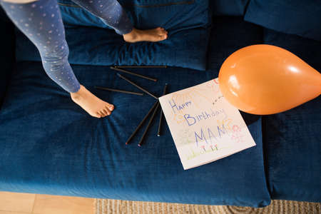 Girl standing at couch near hand drawing greeting picture for her mothers birthday