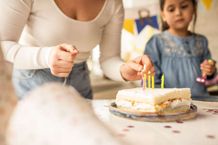 Mother lights the candles on the birthday cake while her daughter standing nearbyの写真素材