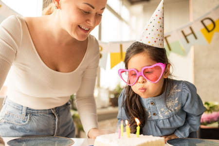 Girl wearing funny glasses blowing candles at the birthday cake while celebratingの写真素材
