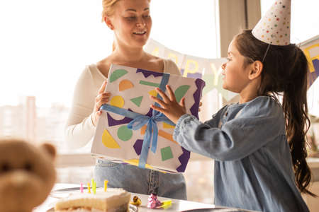 Woman giving a gift to her daughter wearing party cap while spending her birthdayの写真素材