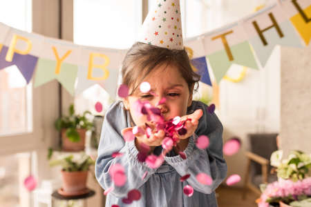 Girl wearing party hat blowing confetti into the camera while celebrating