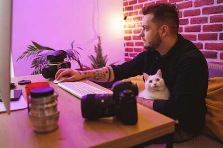 Man retouching photos at the computer with his white cat at the laps