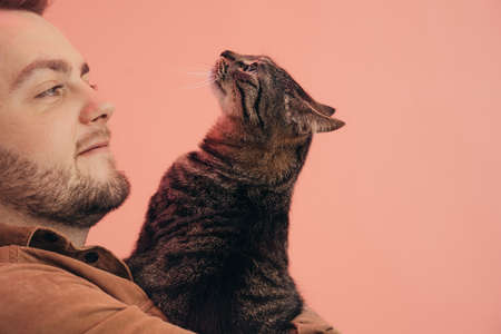 Man holding his striped cat at the hands and looking at him while posingの写真素材