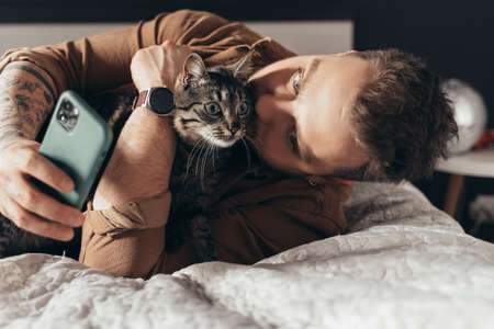 Man laying at the bed with his cat and making selfieの写真素材