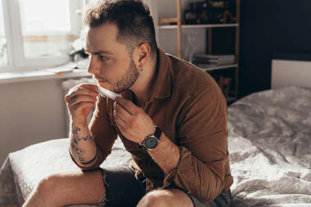 Man sitting at table and rolling with his tongue hand rolled cannabis cigarette