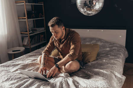 Man sitting at the laptop and typing something while smoking marijuana cigaretteの写真素材