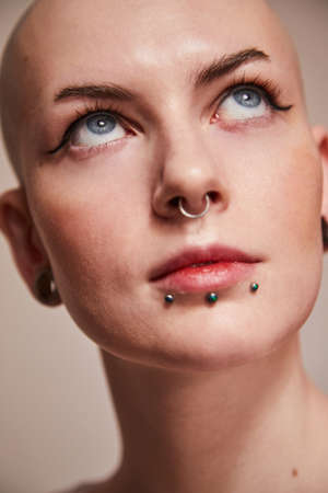 Naked woman with piercing at her face looking up while posing at the studioの写真素材