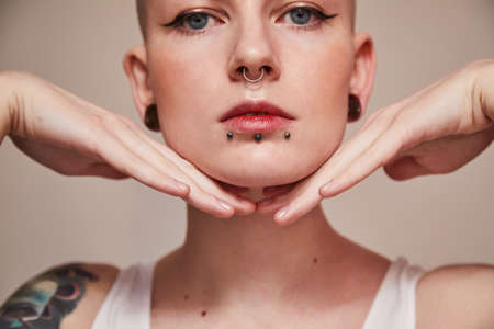 Woman with piercing at her face and ear tunnels posing with hands near her faceの写真素材
