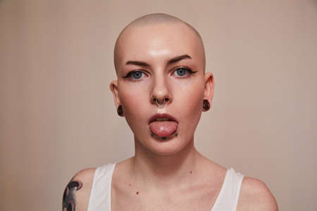 Impudent woman with piercing at her face skin showing her tongue while posing