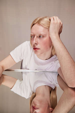 Albino blonde man reflecting at the table while holding head at his handの写真素材