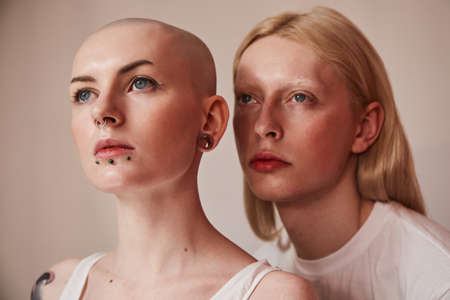 Womanly albino man with long blonde hair posing nearby bald masculine femaleの写真素材