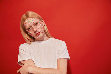 Man with rhinestones at his face and feminine facial features posing at the studio