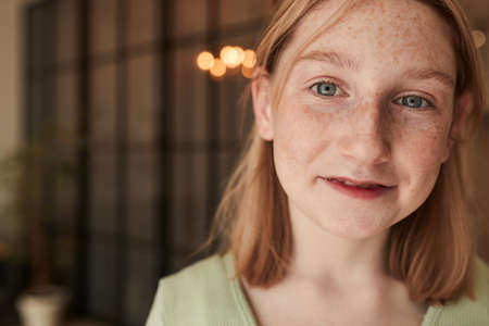 Girl with freckled face looking at the camera while posing at her cozy flat