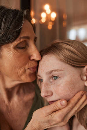 Woman kissing at the forehead her lovely granddaughter while posing to the camera
