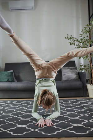 Girl standing at the yoga pose at the carpet and standing at the hands