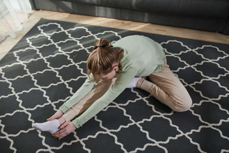Firl sitting at the floor at the carpet and reaching to her leg