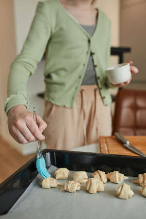 Girl greases bagels with an egg while preparing bakery at the kitchen