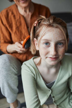 Girl smiling and looking at the camera while her grandmother preparing hairstyle
