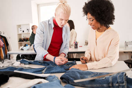 Colleagues cutting clothes while re sewing old products at the tableの写真素材