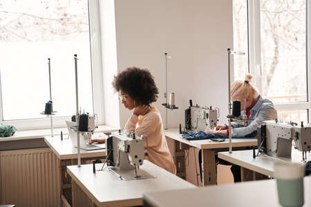 Woman sitting near her sewing machine with laptop and working attentively