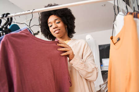 Woman looking at the hangers with clothes while working at the fashion workshopの写真素材
